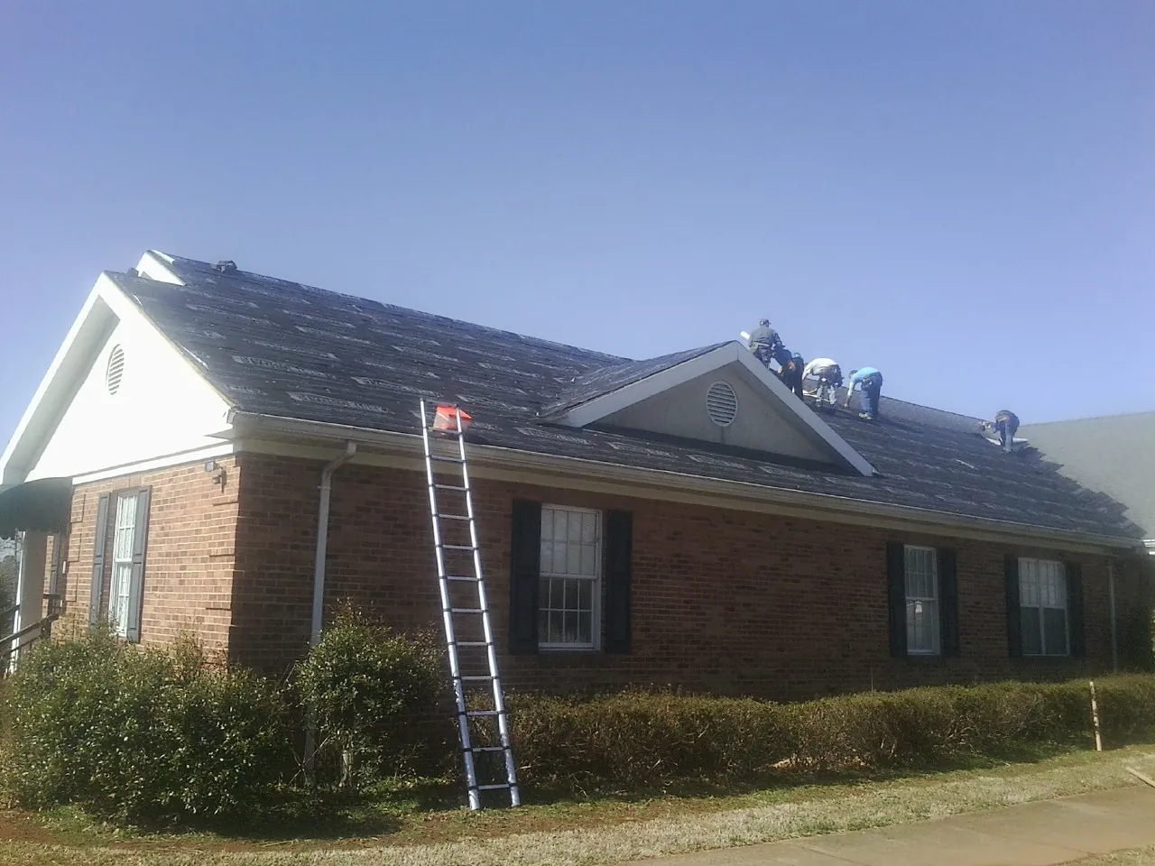 Crew tearing shingles off a brick ranch roof with a ladder set — Emergency Roof Repair work by our crew in Aumsville