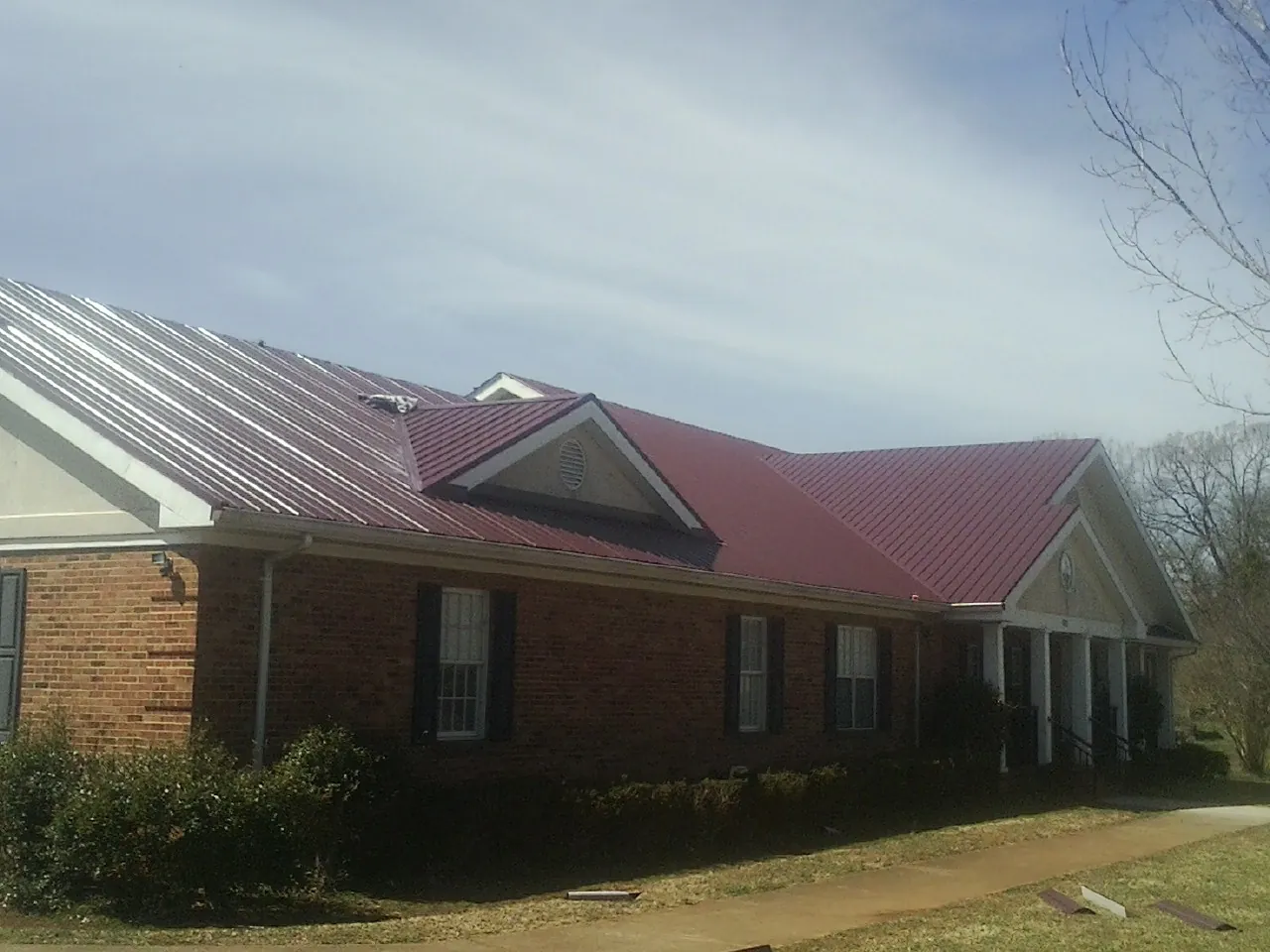 Red metal roof with gabled entries on a long brick building, from a Hail Damage Roof Repair job in Aumsville