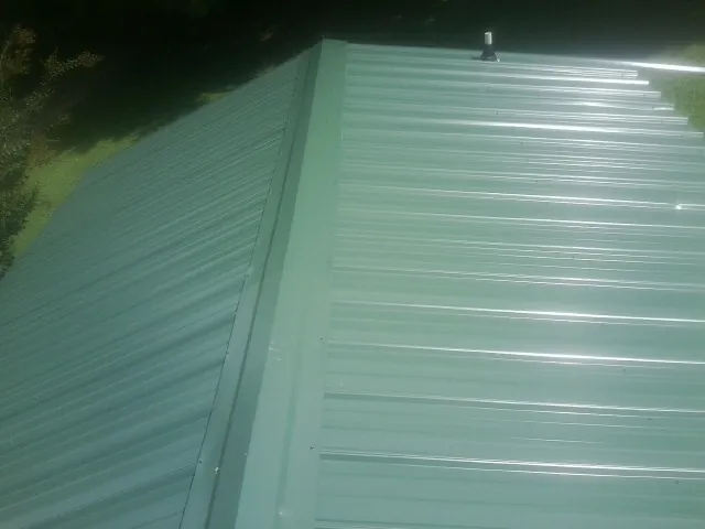 New green metal panels meeting at the ridge of a roof — Flat Roof Repair work by our crew in Aumsville
