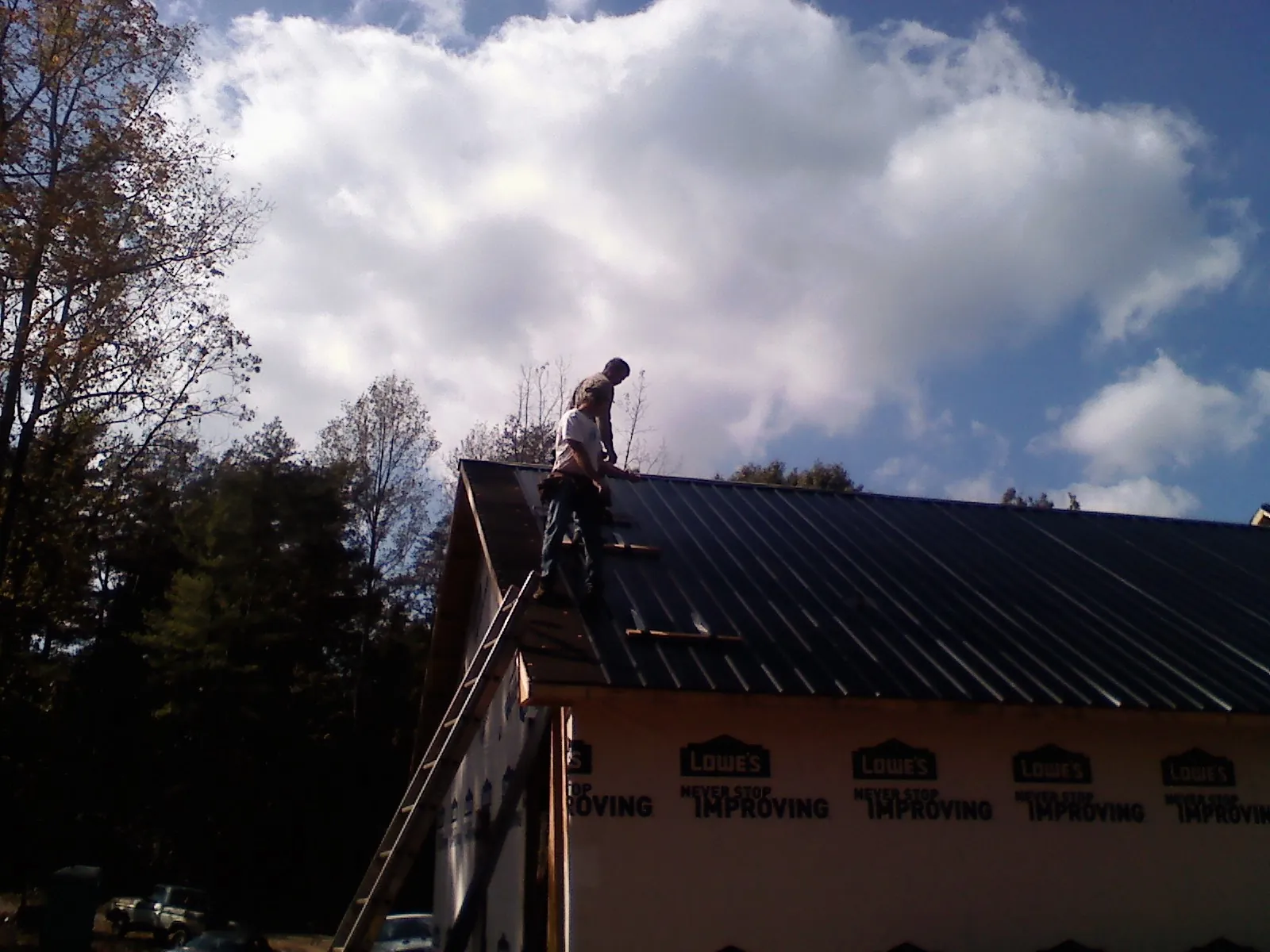 Roofer fastening dark metal panels high against a cloudy sky, from a Roof Inspection job in Aumsville