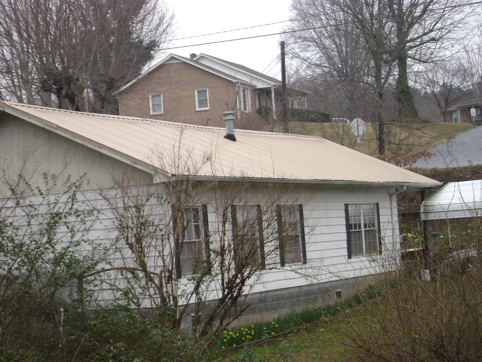 Tan metal roof on a white sided house set into a hillside — Commercial Roofing by Roofing Brothers in Aumsville